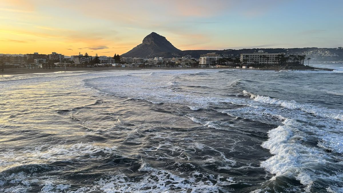 The Arenal bay at dusk, waves rolling in with the Montgó behind the town
