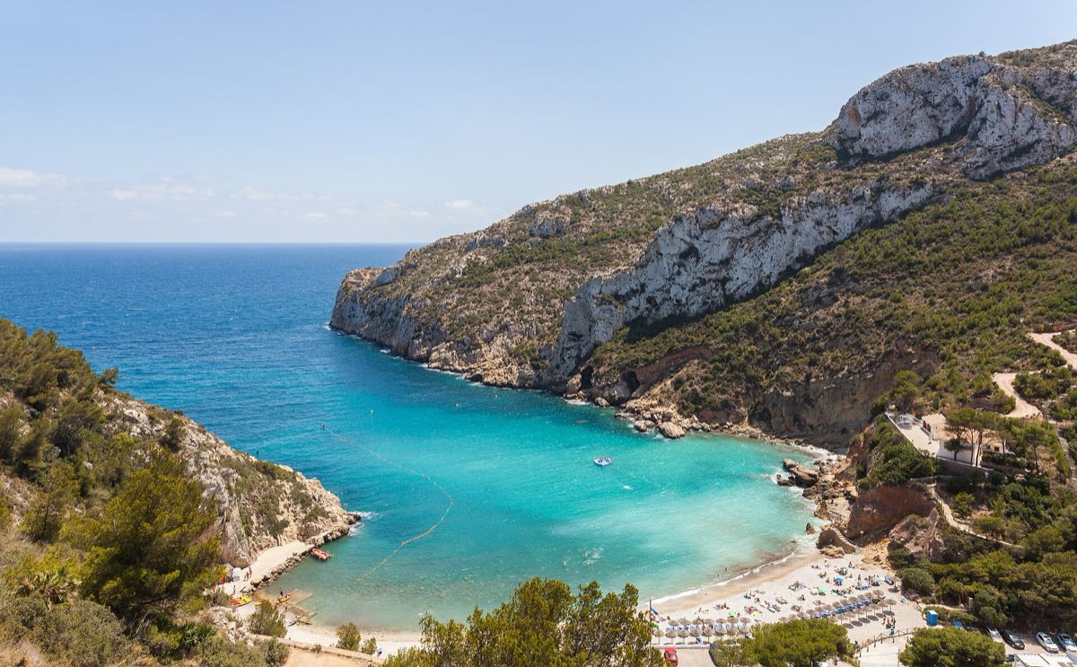 Cala Granadella from above — turquoise water framed by pine-covered cliffs