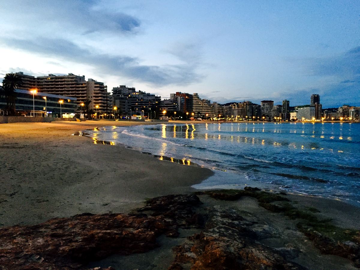 Calpe’s curving seafront at dusk, wet sand reflecting the first promenade lights