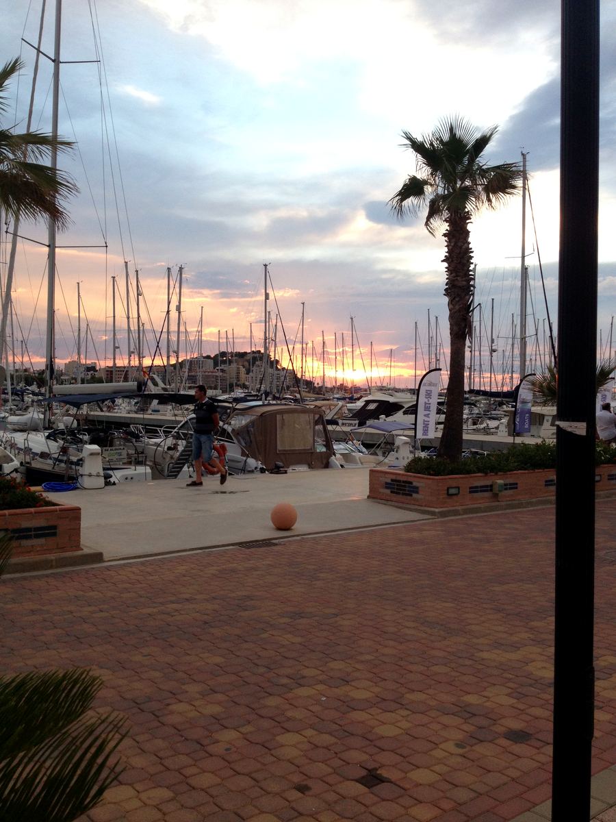 Sailing yachts moored in Dénia’s marina at sunset, palms silhouetted against an orange sky