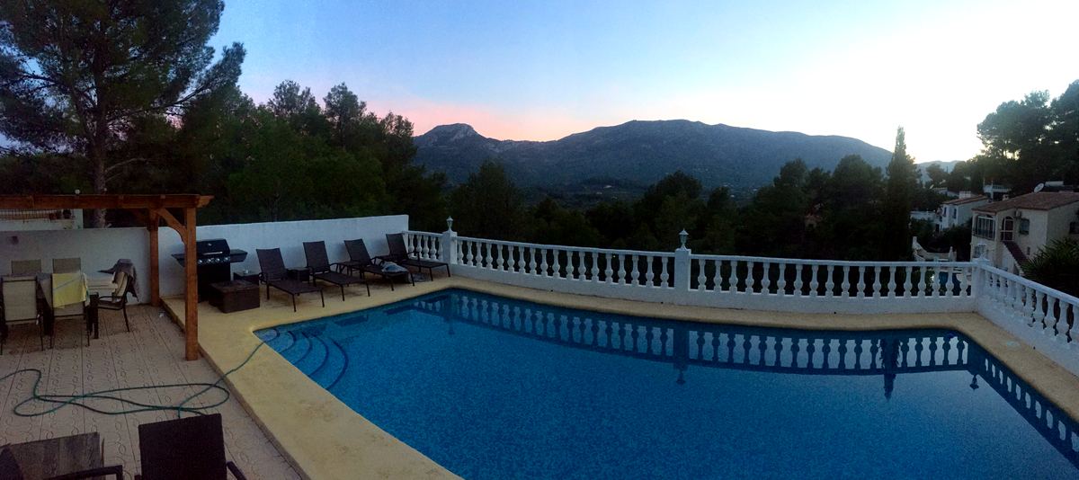 A holiday-villa pool at dusk, sun loungers waiting and the Marina Alta hills fading to pink