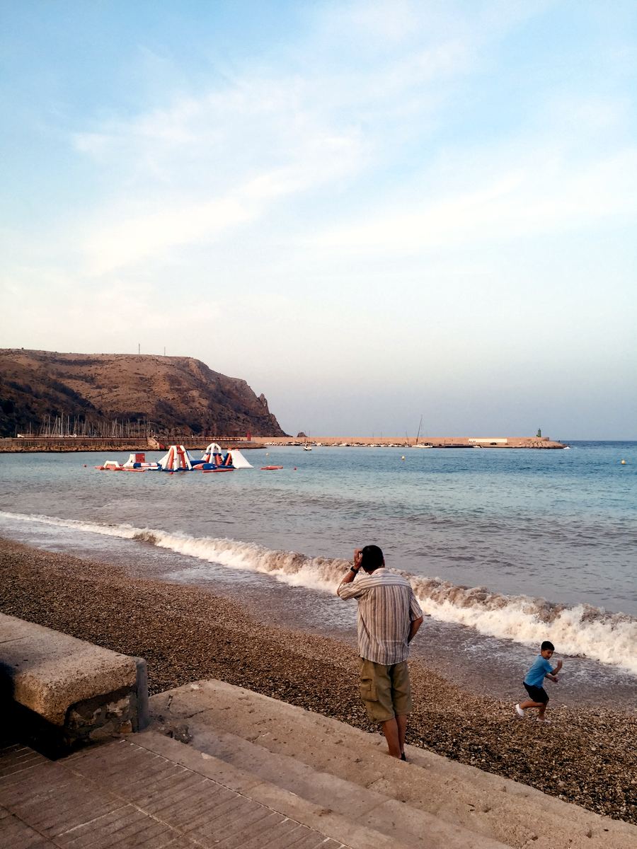 The pebbled La Grava beach by Jávea port with the harbour wall beyond