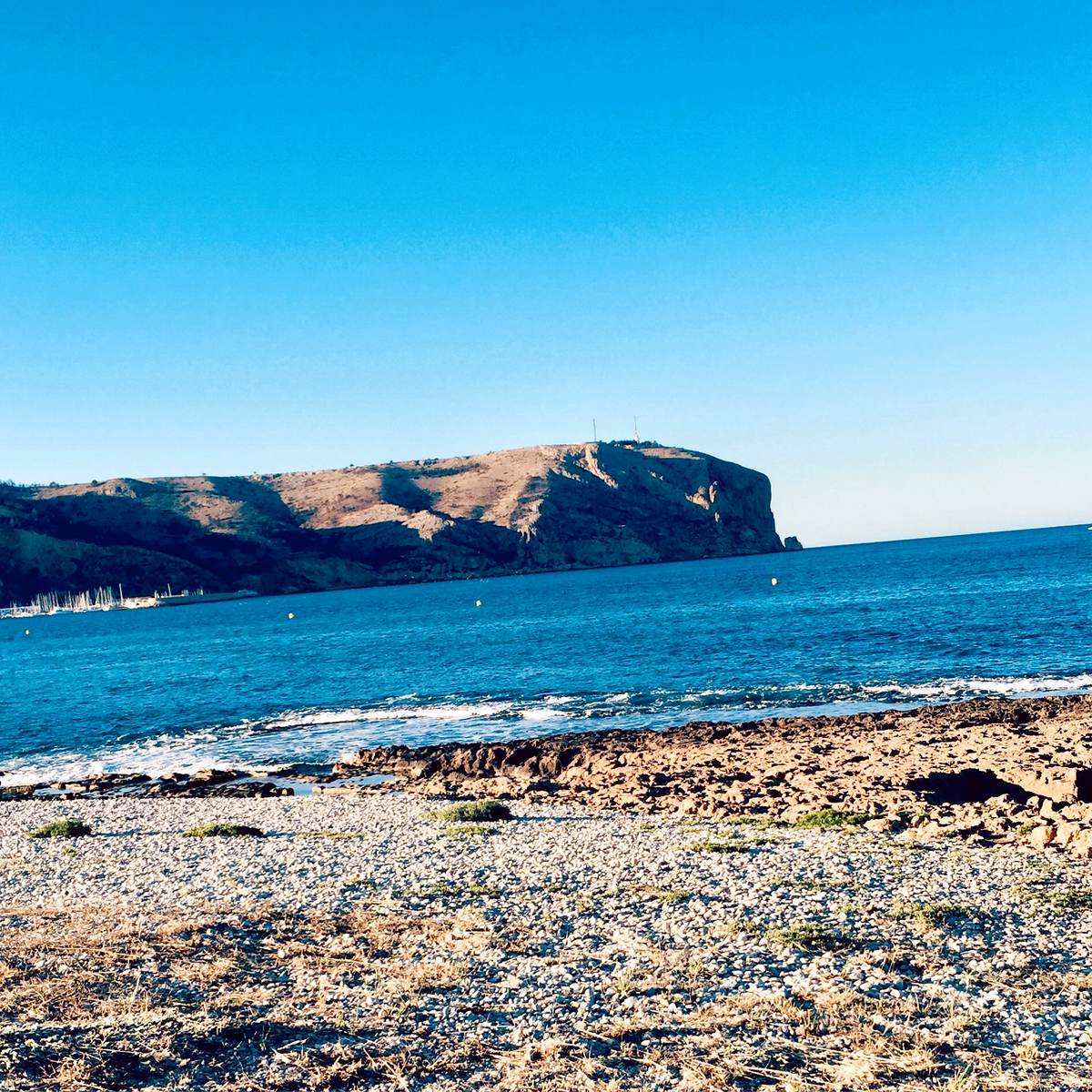 Pebble shore of the Muntanyar with Cap de Sant Antoni across the bay