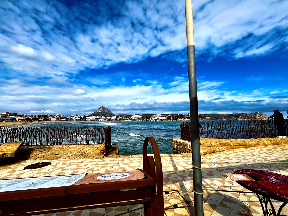 A bench on the paved seafront with the whole bay and Montgó in view