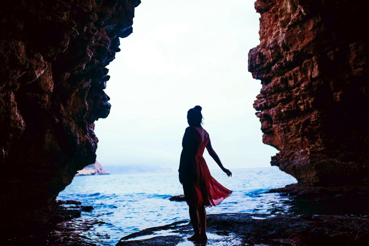 Silhouette at the mouth of a sea cave, dark rock framing the open Mediterranean