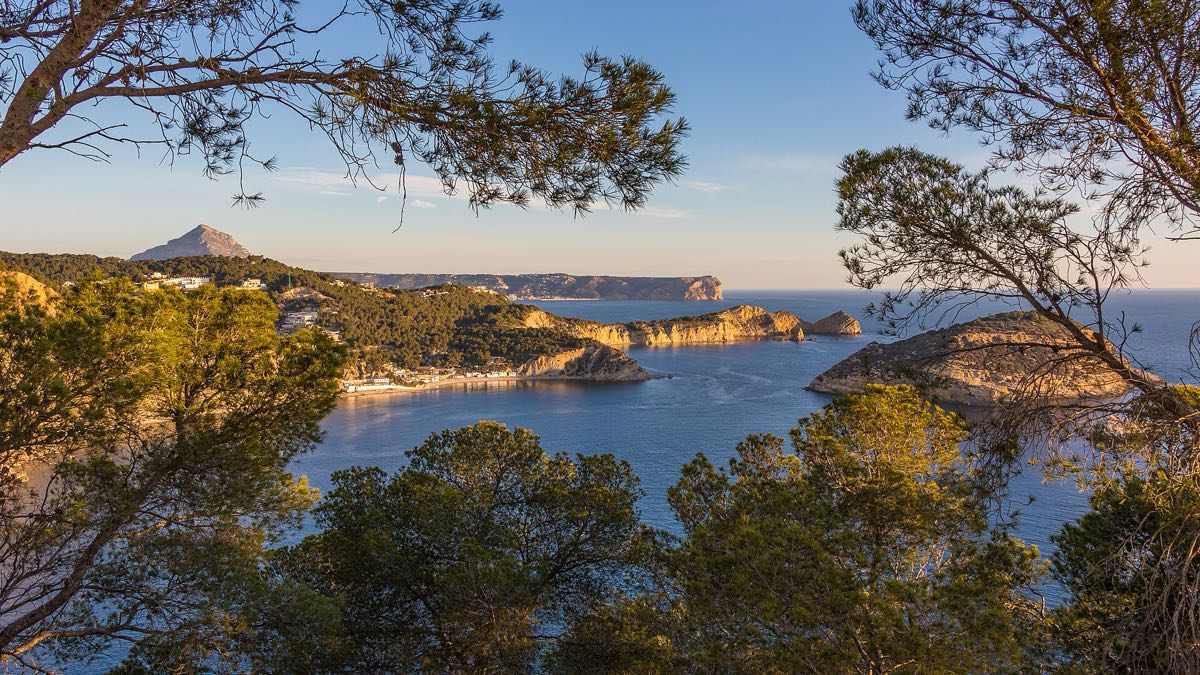 The Portitxol islet and bay seen through pines, with the Montgó on the horizon